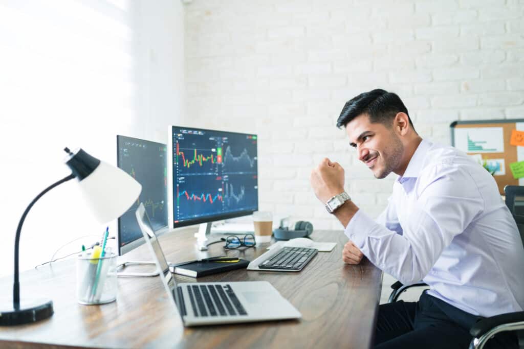 confident handsome hispanic financial broker showing fist computer screen while trading from home